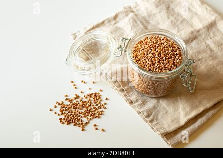 Ein Glas mit Buchweizen und Buchweizen Körner auf dem weißen Tisch verstreut, gesunde und glutenfreie Diät Stockfoto