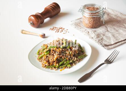 Buchweizenbrei mit grünen Bohnen und Karotten, Buchweizen im Glas auf beiger Serviette, gesunde glutenfreie vegetarische Kost Stockfoto