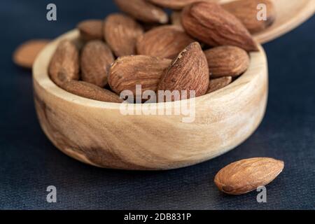 Nahaufnahme von Mandeln in einer Holzschale mit einem Holzlöffel auf einem schwarzen Tisch. Umweltfreundliches Konzept Stockfoto