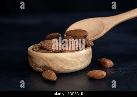 Mandeln in einer Holzschale mit einem Holzlöffel auf einem schwarzen Tisch. Nahaufnahme und minimalistische Aufnahme Stockfoto