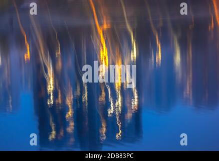 Silhouetten mehrstöckiger Häuser mit hellem Licht in den Fenstern spiegeln sich auf der blauen Wasseroberfläche im See. Große Stadt im Detail Stockfoto