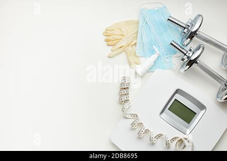 Sportgeräte, Waagen, medizinische Masken und Desinfektionsmittel auf weißem Hintergrund. Draufsicht, Kopierbereich. Fitness. Ausgabezeitraum. Gewicht und Gesundheitskontrolle Stockfoto