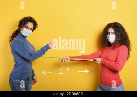 Freunde halten Abstand zwischen ihnen von 1 Meter. Konzept der codiv-19-Regeln zur Vermeidung einer Pandemie. Gelber Hintergrund. Stockfoto