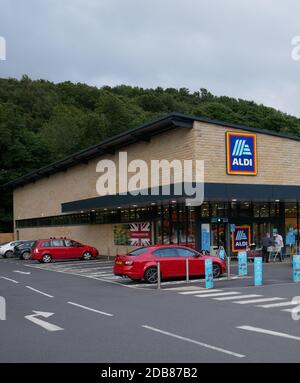 Aldi Stein gebaut Supermarkt Eingang blau gelb weiß und rot schild Trolleys Zebra Kreuzung geparkten Autos und Straße Stockfoto