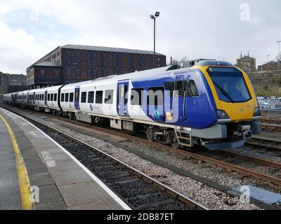 Gelb blau und silber Mehrwagen Eisenbahn-Zug geparkt Bahnhof rotes Backsteingebäude im Hintergrund Stockfoto