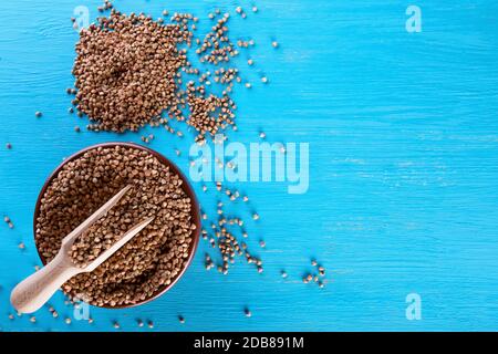 Tonschale mit Buchweizen und einem Holzspatel auf blauem Hintergrund. Blick von oben. Das Konzept der gesunden natürlichen Lebensmitteln. Stockfoto