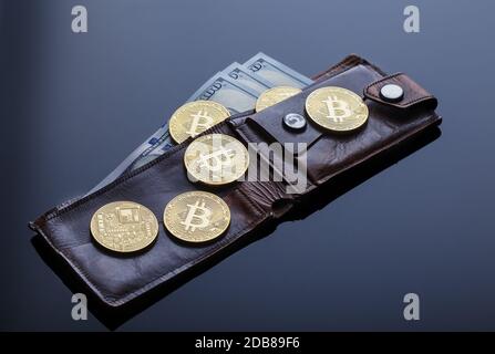 Geldbörse mit Goldbitcoins und hundert Dollar-Scheinen auf dunklem Hintergrund. Das Konzept des virtuellen Geschäfts und der Währung. Stockfoto
