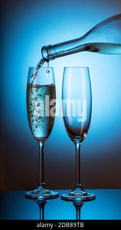 Champagner wird in eines von zwei Gläsern auf blauem Grund gegossen Stockfoto