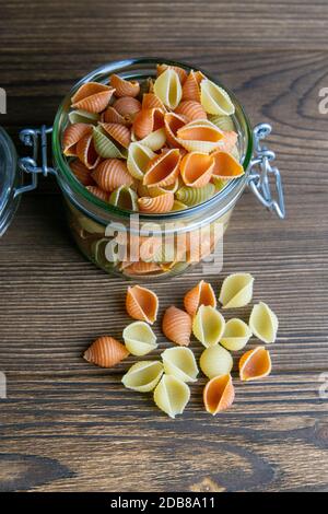 Bunte Conchiglie Pasta in Glas Glas auf Holzhintergrund. Vorderansicht, Nahaufnahme. Stockfoto