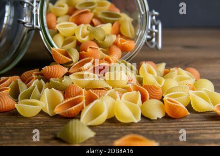 Bunte Conchiglie Pasta in Glas Glas auf Holzhintergrund. Vorderansicht, Nahaufnahme. Stockfoto