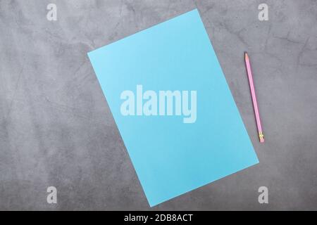 Flaches Lay, Draufsicht, blaues Blatt und Bleistift auf grauem, strukturiertem Hintergrund. Lichtstrahlen von der Seite Stockfoto