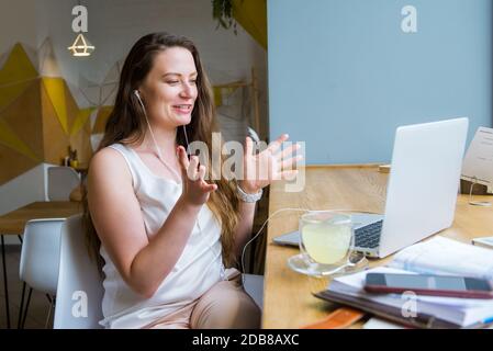 Lächelnde Geschäftsfrau in Headsets mit einem Videoanruf Chat auf ihrem Laptop sitzen im Café, Coworking. Remote-Arbeit, soziale Netzwerke, Blogging Stockfoto
