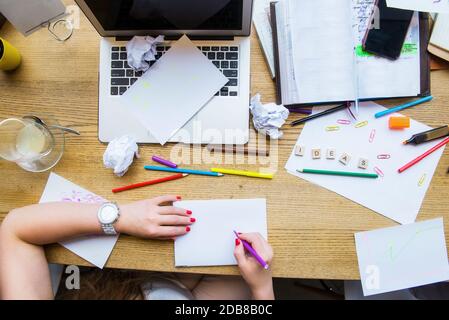 Draufsicht weibliche Hände halten Stift über weißem leeren Notizbuch für neue kreative Ideen. Arbeitsplatz mit Laptop, Rohlingen, buntem Briefpapier und Ideen Stockfoto