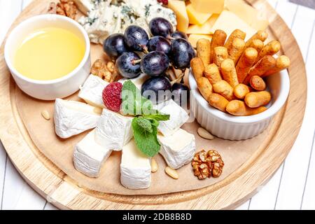 Brett mit verschiedenen Käsesorten. Käse Mischung Set dor blu chedar Parmesan Brie Honig Sauce Fingerbrot und Trauben auf Wooren Parte. Frühstücksteller auf der Speisekarte des Restaurants. Gesundes Snacksortiment Stockfoto