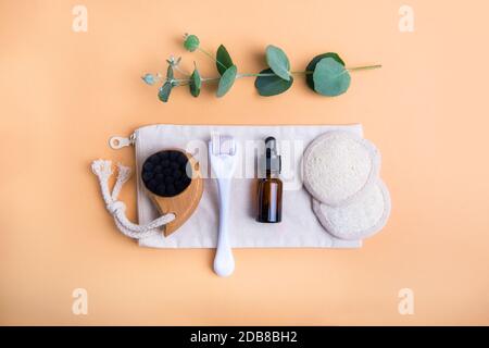 Home Self-Care-Kit für Gesichtsmassage. Trockene Lymphdrainage Pinsel, Derma mezoroller, Loofah Pads, natürliches Öl Serum und Eukalyptus auf beigem Hintergrund Stockfoto