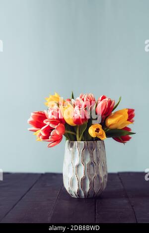 Frisches frühlingsgelbes und rosa Tulpen Bouquet in Vase stehend auf schwarzem Holztisch mit graublauem Hintergrund. Festliche Blumen für Mutter oder Frauen Stockfoto