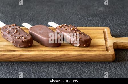 Schokoladenbedeckte Vanilleeissägel auf dem Holzbrett Stockfoto