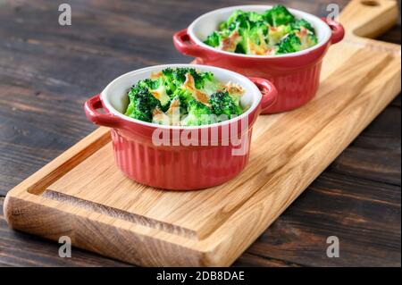 Zwei Töpfe mit gebackenem Brokkoli und Käse auf Holzbrett Stockfoto