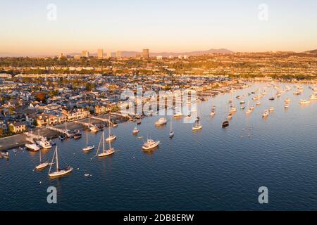 Luftaufnahme der Boote in Newport Beach Hafen mit verankert Balboa Island und die weit entfernte Skyline im goldenen Schein des Sonnenuntergangs Stockfoto