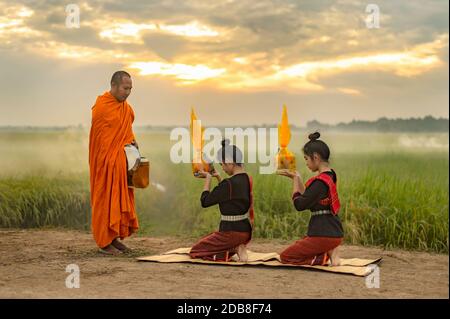 Zwei Frauen knien vor einem Mönch, der Almosen anbietet, Thailand Stockfoto