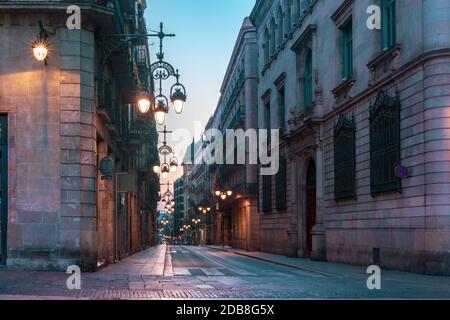 Enge gepflasterte, leere Straße aus dem Mittelalter mit schöner Straßenbeleuchtung im gotischen Viertel Barri am Morgen, Barcelona, Katalonien, Spanien Stockfoto