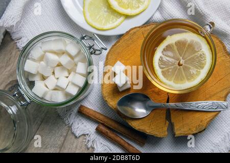 Glas transparente Tasse mit Minztee steht auf einem Holzständer, neben einer Zuckerdose mit Zuckerwürfeln, in Scheiben geschnittene Zitrone und einem Löffel. Stockfoto