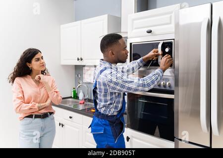 Glückliche junge Frau, die in der Nähe von Techniker Einstellen der Temperatur von Backofen stehen Stockfoto