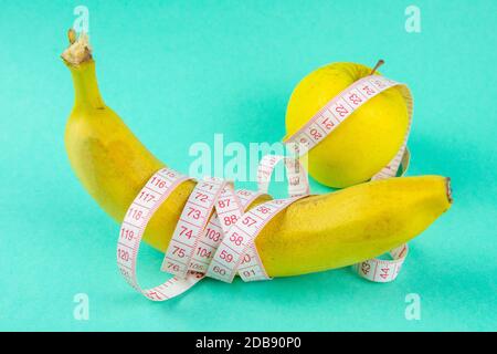 Verschiedene Arten von Obst, wie Äpfel und Bananen liegen auf einem Fuß und sind in einem Maßband verpackt - Konzept für eine gesunde Gewichtsabnahme Stockfoto