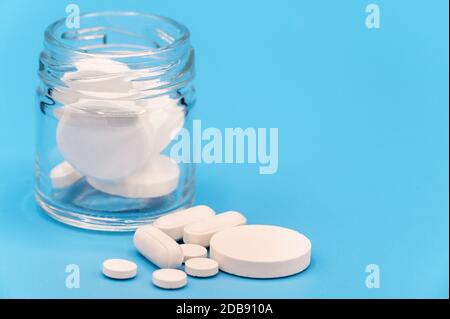 Nahaufnahme der Pillen, die aus der Pillenflasche auf blauem Hintergrund verschüttet wurden. Mit Kopierraum. Medizinkonzept . Stockfoto