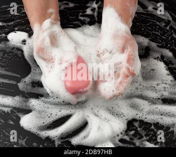 Prozess der Händewaschen mit rosa Seife, Teile des Körpers in weißem Schaum auf schwarzem Hintergrund, Draufsicht, Hygiene-Konzept Stockfoto