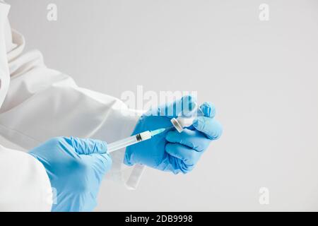 Arzt mit Impfstoff und Spritze in den Händen, blaue OP-Handschuhe, weißer Hintergrund. Stockfoto