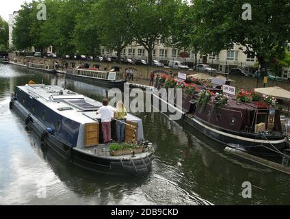 Ein Kanal boal passiert das schwimmende Waterside Cafe Kanalboot Und zwei Wasserbus-Touristenboote, die zwischen Klein-Venedig fahren Und Camden in London's lit Stockfoto