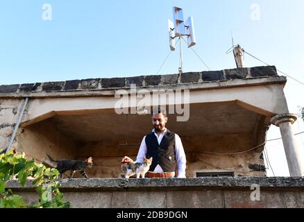 Sweida, Syrien. November 2020. Diaa Abdullah, ein 31-jähriger Ingenieur, spielt am 2. November 2020 mit seinen Katzen unter einer Windturbine, die auf dem Dach seines Hauses in der Provinz Sweida, im Süden Syriens, installiert ist. Quelle: Ammar Safarjalani/Xinhua/Alamy Live News Stockfoto