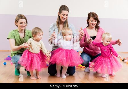 Drei Mädchen in rosa Röcken lernen mit zu gehen Hilfe ihrer Mütter Stockfoto