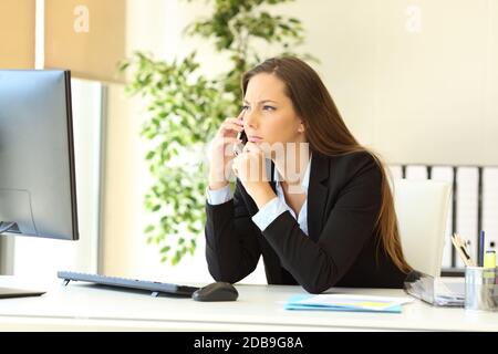 Nachdenkliche Führungskraft, die im Büro mit Computer am Smartphone spricht Stockfoto