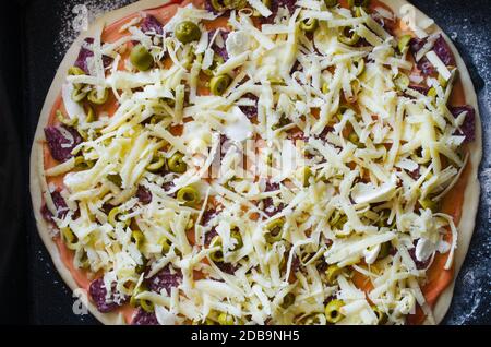 Hausgemachte rohe Pizza mit Salami, Mozzarella, Oliven und Käse. Draufsicht. Nahaufnahme Stockfoto