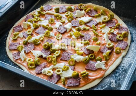 Hausgemachte rohe Pizza mit Salami, Mozzarella, Oliven und Käse. Nahaufnahme Stockfoto