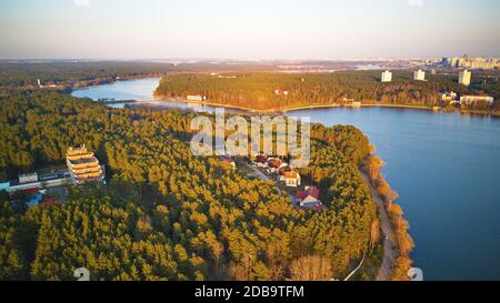 Erholungszone und große Stadt Luftaufnahme. Flussufer mit Wald und Sanatorium im Frühling Sonnenlicht. Der Aprilabend am See neben Minsk, Weißrussland. Beau Stockfoto