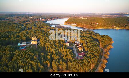 Erholungszone und große Stadt Luftaufnahme. Flussufer mit Wald und Sanatorium im Frühling Sonnenlicht. Der Aprilabend am See neben Minsk, Weißrussland. Beau Stockfoto