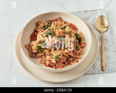 Pasta Farfalle mit Tomatensauce und gemahlenem Fleisch in Teller auf weißer Marmorplatte. Idee und Rezepte für einfache, einfache Mittag-oder Abendessen ein-Topf-Fleisch Gou Stockfoto