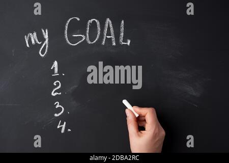 Hand hält ein weißes Stück Kreide auf dem Hintergrund einer Kreidetafel mit der Aufschrift mein Ziel Stockfoto