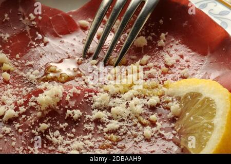 Brosaola-Scheiben mit Zitronensaft, Olivenöl und Parmesankäse. Stockfoto