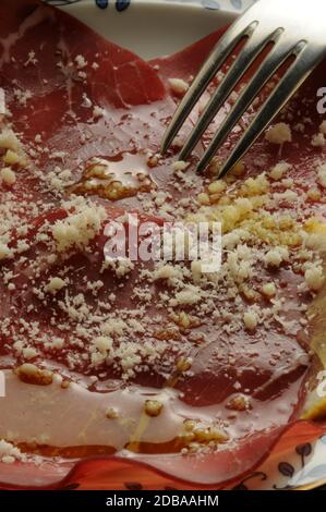 Brosaola-Scheiben mit Zitronensaft, Olivenöl und Parmesankäse. Stockfoto