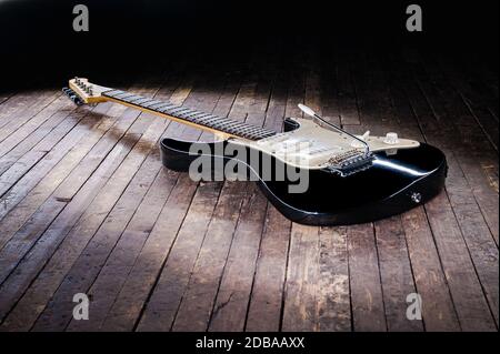 Schwarz-weiße E-Gitarre mit gelbem Signaturstempel liegt auf einer Holzbühne Stockfoto