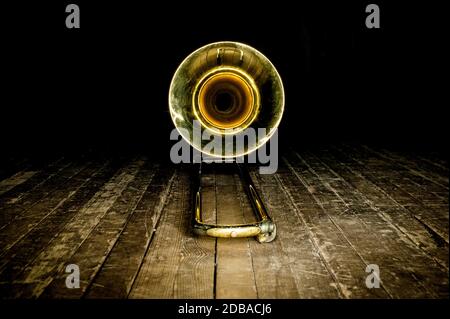 Auf dem Holzboden der Bühne liegt die Posaune aus gelbem Blechblasinstrument, auf der Glocke die Vorderansicht Stockfoto