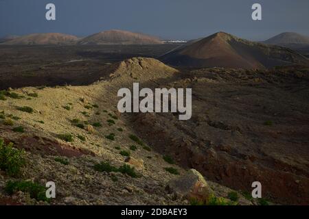 Wunderschöne Vulkanlandschaft am frühen Morgen auf Lanzarote, Spanien. Der Calima Wind macht ein surreales Licht. Weit hinten die kleine Stadt Manc Stockfoto