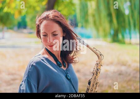 Nahes Porträt einer jungen rothaarigen Frau in einem grünen Park mit Saxofon im Sommer Stockfoto