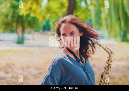 Nahes Porträt einer jungen rothaarigen Frau in einem grünen Park mit Saxofon Stockfoto