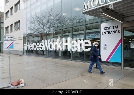 Ein Krankenhauspersonal mit Gesichtsmaske kommt an einem Schild vorbei, das die Mitarbeiter des Gesundheitswesens vor dem Eingang des Mount Sinai Hospitals in Astoria, Queens, unterstützt. Stockfoto
