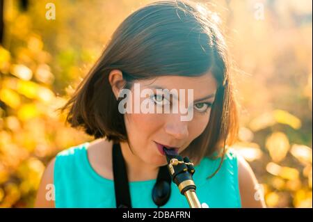 Porträt einer niedlichen jungen Saxophonistin mit schwarzen Haaren in blauer Kleidung auf gelbem Hintergrund Stockfoto